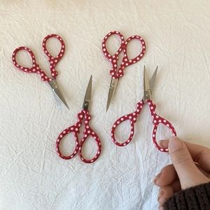 Macro shot of mini stainless steel craft scissors with red polka dot handles held by hand