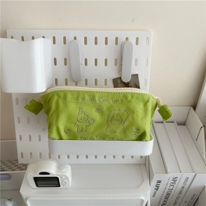 Green canvas pencil case with cute rabbit embroidery and zip closure on storage shelf