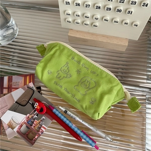 Detail of green canvas pencil case featuring cartoon embroidery and secure zipper