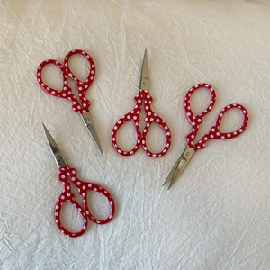 Detailed view of four mini red polka dot embroidery scissors on white fabric