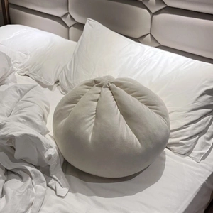 Creative dumpling-shaped plush pillow in creamy white on a cozy white bed setting