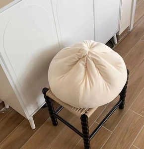 Close-up of a soft cream dumpling plush pillow with pleated texture on a woven stool