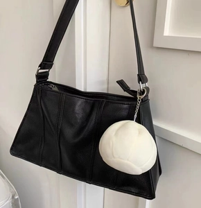 Close-up of black textured leather shoulder bag with a soft white cloud plush pendant