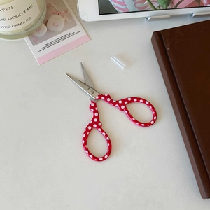 Close-up of red polka dot mini stainless steel scissors with protective cap on desk