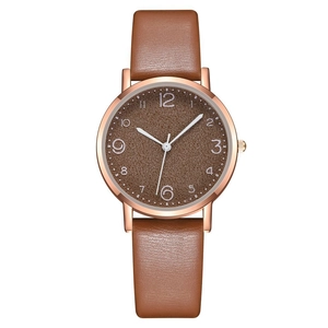 Detail of brown leather strap and rose gold watch case with arabic numeral dial
