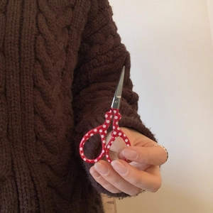 Detailed close-up of mini red polka dot scissors held in hand for precision embroidery