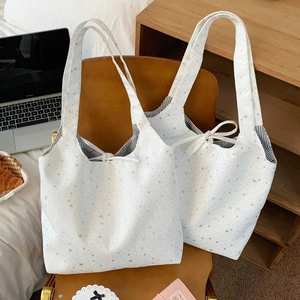 Detail of white star print tote bag with striped lining and tie closure on brown chair