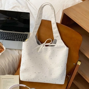 White canvas tote bag with star prints featuring a drawstring closure in a lifestyle setting