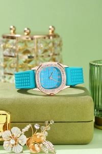 Detail of teal silicone strap and rose gold rhinestone square watch on velvet stand
