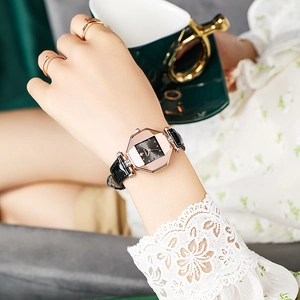 Close-up of elegant rose gold octagonal watch with black leather strap and green coffee cup