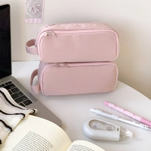 Close-up of pink portable stationery bag with dual zippers and handle on a study desk