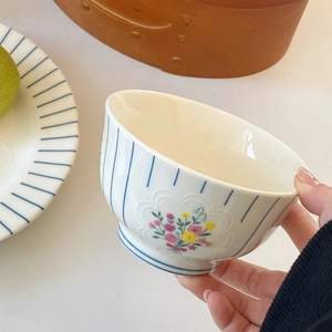 Close-up of hand holding a ceramic bowl with blue stripes and floral pattern