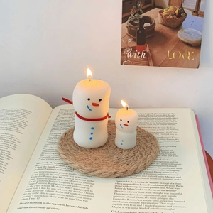 Close-up of cute snowman scented candles on a woven coaster with a festive cozy backdrop