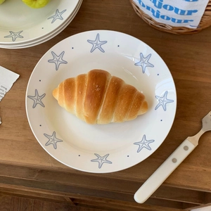Detail of a white ceramic plate with blue starfish pattern featuring a golden croissant