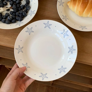 Close-up of a white ceramic plate with blue starfish motifs on a rustic wooden table