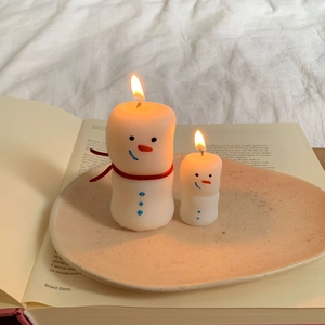 Close-up of small and large snowman scented candles with red scarves on a ceramic tray