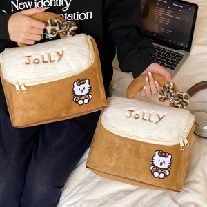 Detail of suede makeup bags featuring cat embroidery and leopard print bows on a bed