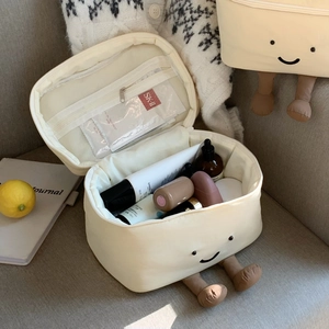 Detail der cremefarbenen Kosmetiktasche mit Smiley-Stickerei und mehrlagigem Stauraum