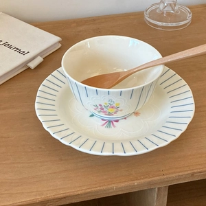Vintage floral ceramic tableware set with blue striped rim and wooden spoon on wooden table