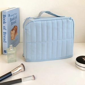 Detailed view of light blue quilted cosmetic bag with vertical stitching and fabric handle