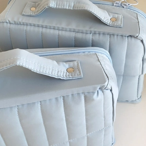 Detail of light blue quilted toiletry bag with golden metal studs and top handle