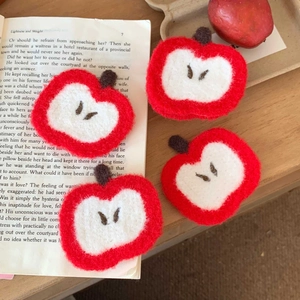 Detailed view of four handmade red felt apple decorations on a vintage book background