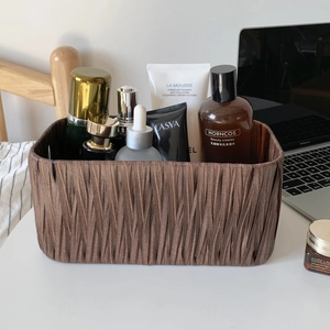 Detail of brown woven storage basket with skincare items on a clean white desk