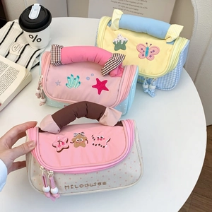 Detail of embroidered canvas pencil cases with wide handles and cute pom decorations