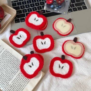 Close-up of red apple hair grips showing plush texture and striped fabric backing detail