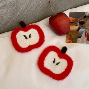 Close-up of handmade crochet apple coasters with soft plush texture on white bedding