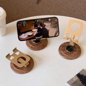 Detail of walnut wood base and rotating gold metal phone stand in a home office setup