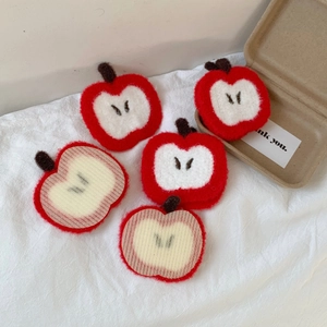 Detailed view of 5 red knitted apple hair clips and packaging on white fabric