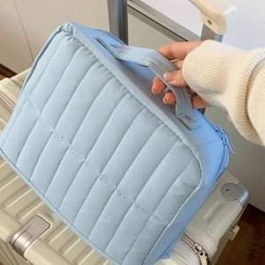 Light blue quilted travel toiletry bag with vertical stripes and top handle on luggage