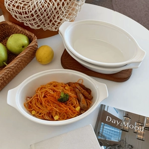Detail of white ceramic oval baking dish with double handles and wooden base tray