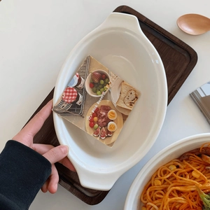 White ceramic oval baking dish with double handles on a wooden tray for salad or dessert