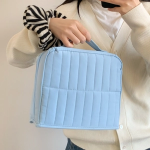 Close-up of light blue quilted toiletry bag featuring vertical stripe texture and handle
