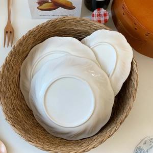 Detail of white ceramic dinner plates with scalloped edges stacked in a woven basket