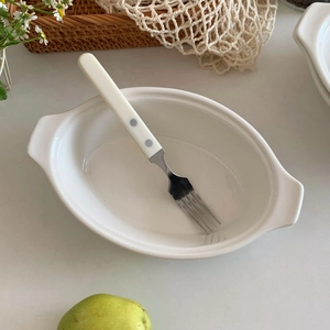 Detail of white ceramic oval dish with handles and polka dot fork in minimalist setting