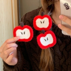 Detail of plush apple slice hair accessories showing red and white knit textures on braids