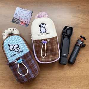 Close-up of plush DJI Pocket 3 storage bags with Lucky Puppy embroidery on wood