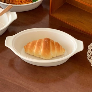 Close-up of white oval ceramic baking dish with handles on a rustic wooden table