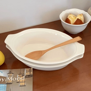 Close-up of a white oval ceramic baking dish with ergonomic double handles on a wooden table