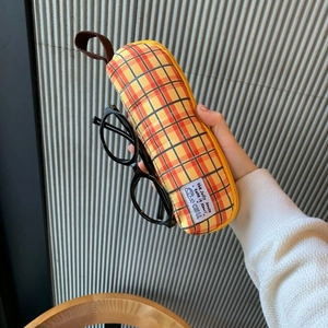 Detail of yellow checkered pencil case with hand placing black glasses inside the pouch
