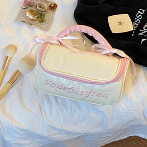 Détail de la trousse à maquillage crème avec nœud rose, fermeture éclair et broderie