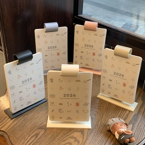 Five assorted colors of 2026 desk calendars with minimalist illustrations on wood table