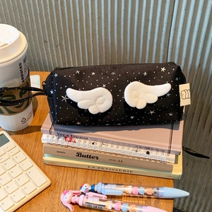 Detail of black star print pencil case with white plush wings and zipper pull cord