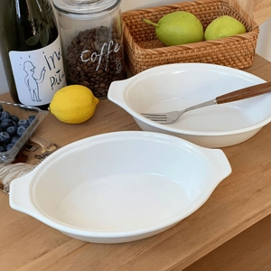 Detailed close-up of white ceramic oval baking dishes with handles on a wooden table