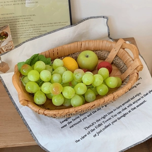 Detail of hand-woven oval rattan fruit basket with side handles in a cozy home setting