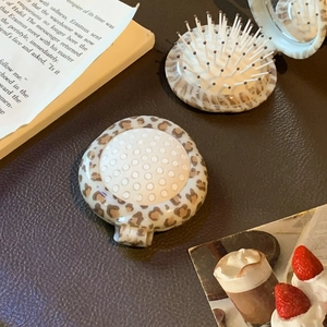 Close-up of portable leopard print folding hair brush with compact mirror on leather background