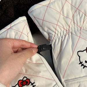 Detail of white quilted ski gloves featuring cartoon cat embroidery and red contrast stitching